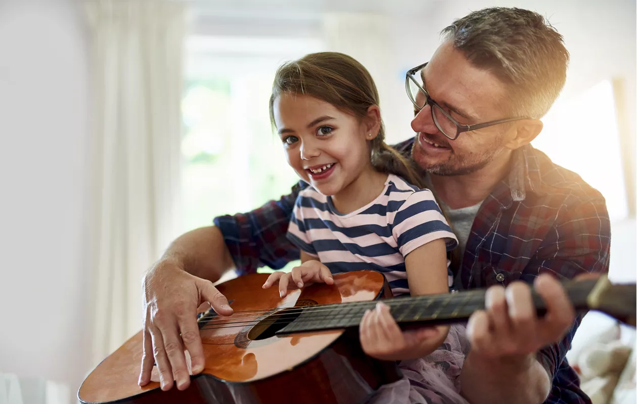 pikkutyttö istuu kummisedän sylissä ja opettelee kitaran soittoa