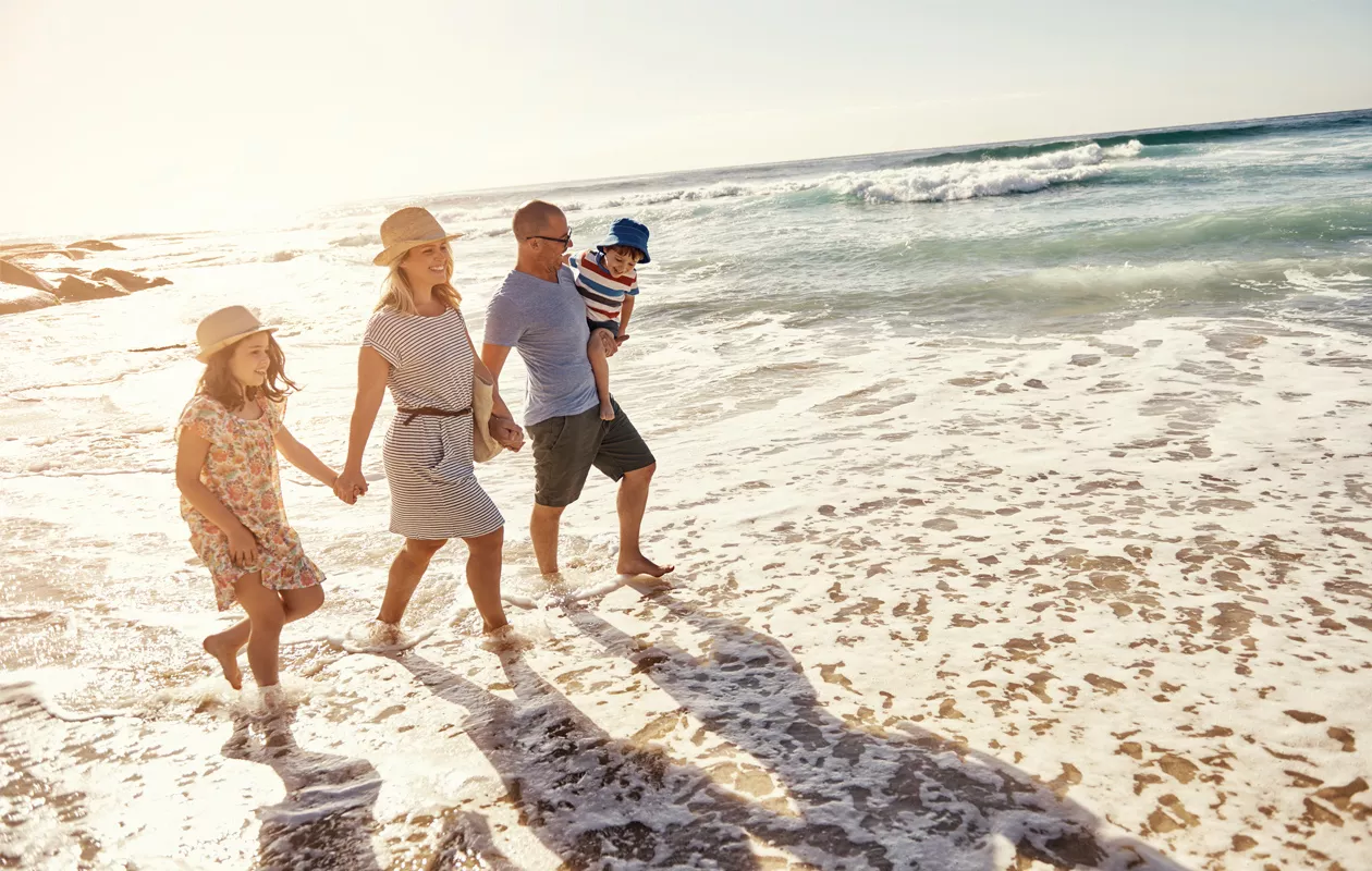 Äiti, isä, tytär ja poika kävelemässä meren rannalla