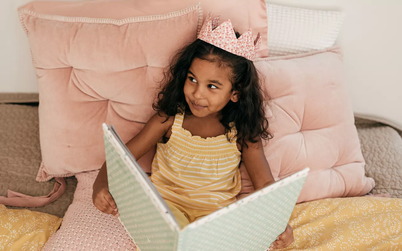 Prinsessasatu - tyttö lukee kirjaa kruunu päässään.