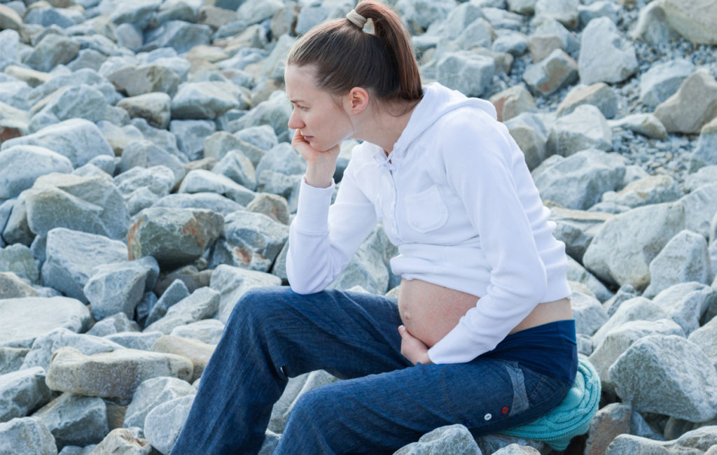 Raskaus ahdistaa: Raskaana oleva, masentunut nainen istumassa rannalla.