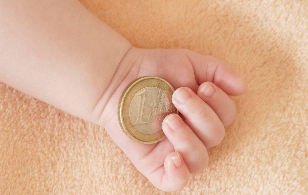 Vauva pitää euron kolikkoa kädessään. Äitiysvapaa, äitiysraha.