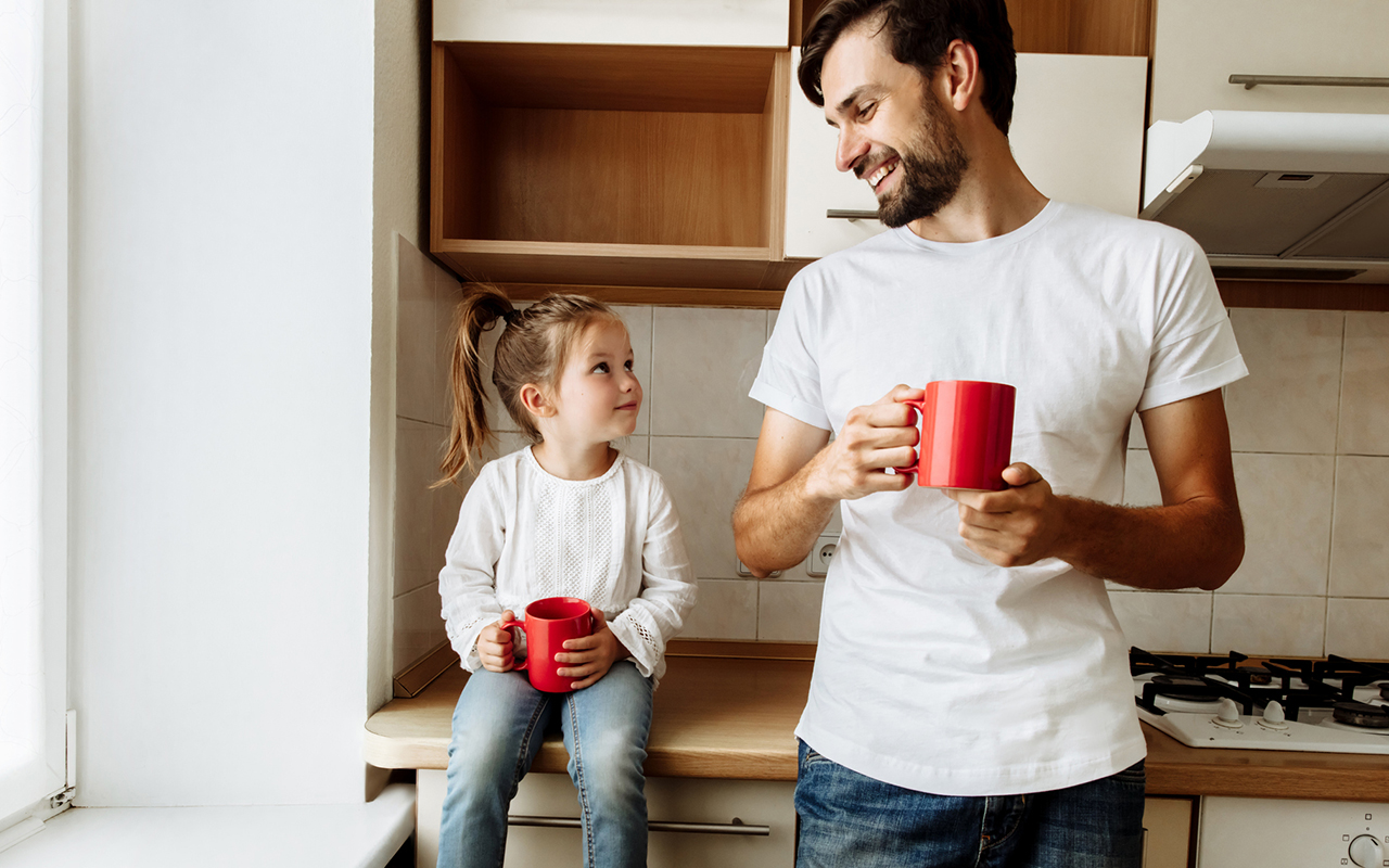 Lapsen raivokohtaukset eivät ole helppoja vanhemmille. Kasvattajavanhempi on jämpti mutta lempeä ja turvallinen. Kuvassa isä hymyilee tyttärelleen, kun he juovat kaakaota keittiössä.