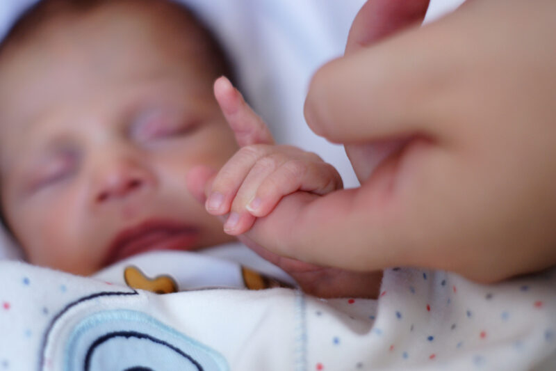kuva vauvasta, joka tarraa nyrkillä aikuisen sormeen