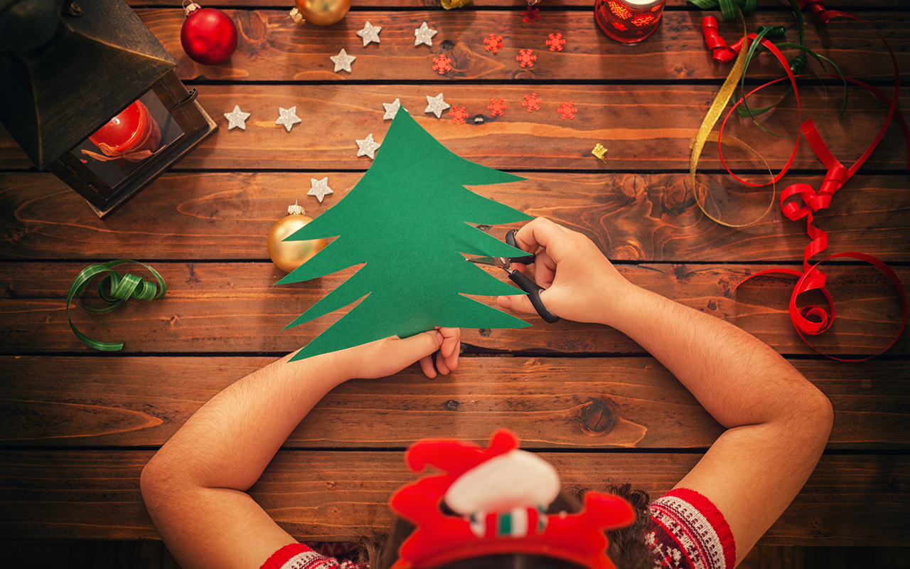 Joulukorttien askartelu lasten kanssa: lapsi leikkaa kartonkikuusta.