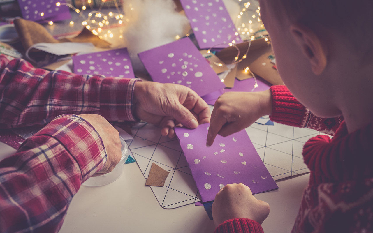 Joulukorttien askartelu lasten kanssa: lapsi taiteilee sormiväreillä lumisadetta.