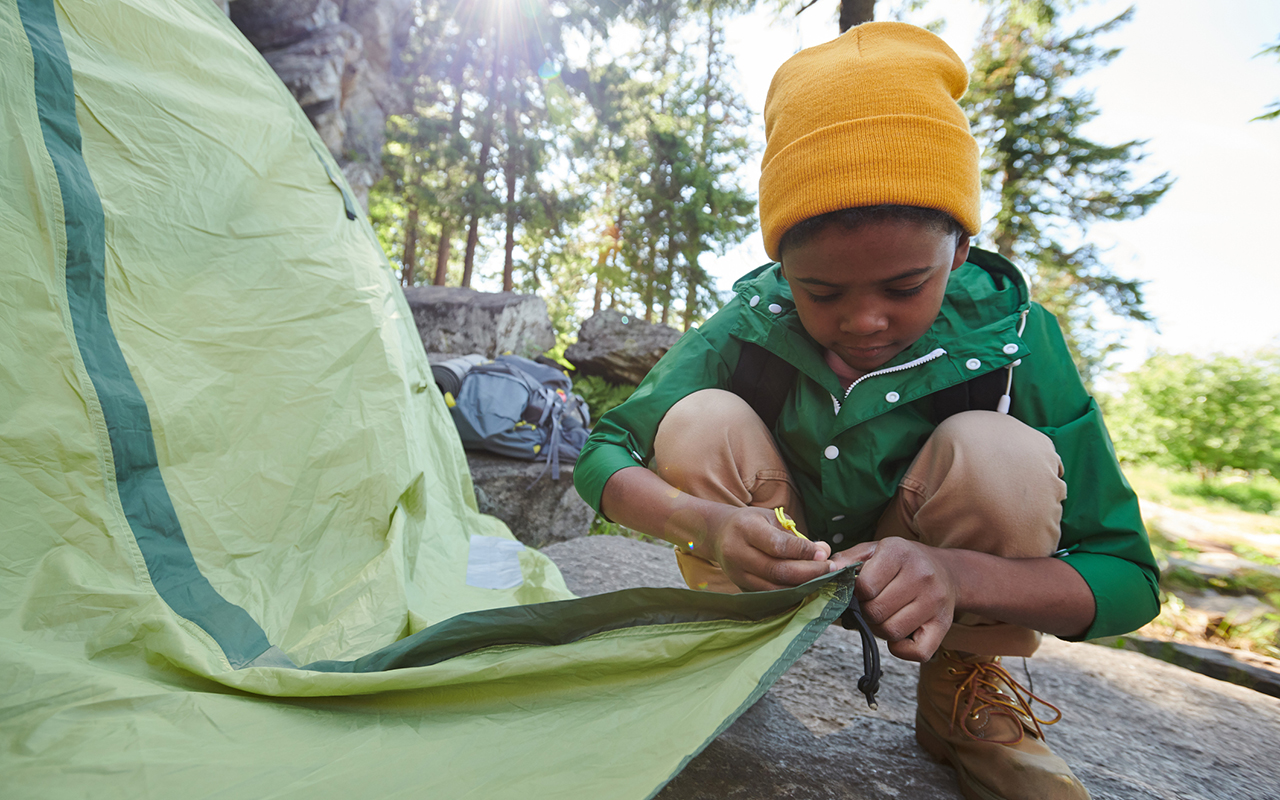Lasten vaelluskengät - poika pystyttää telttaa leirissä.