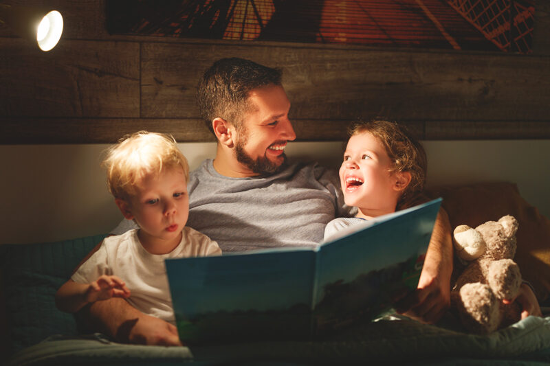 Isä lukee lapsille sängyssä
