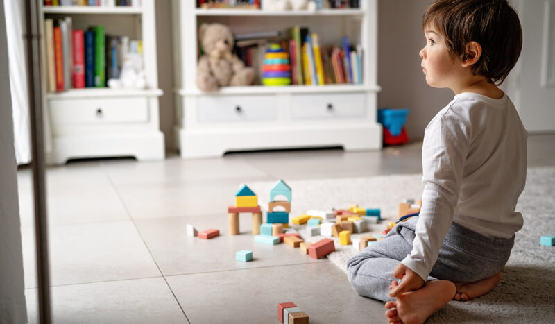 leikkiatidto: lapsi istuu lattialla lelujen keskellä ja katsoo ulos