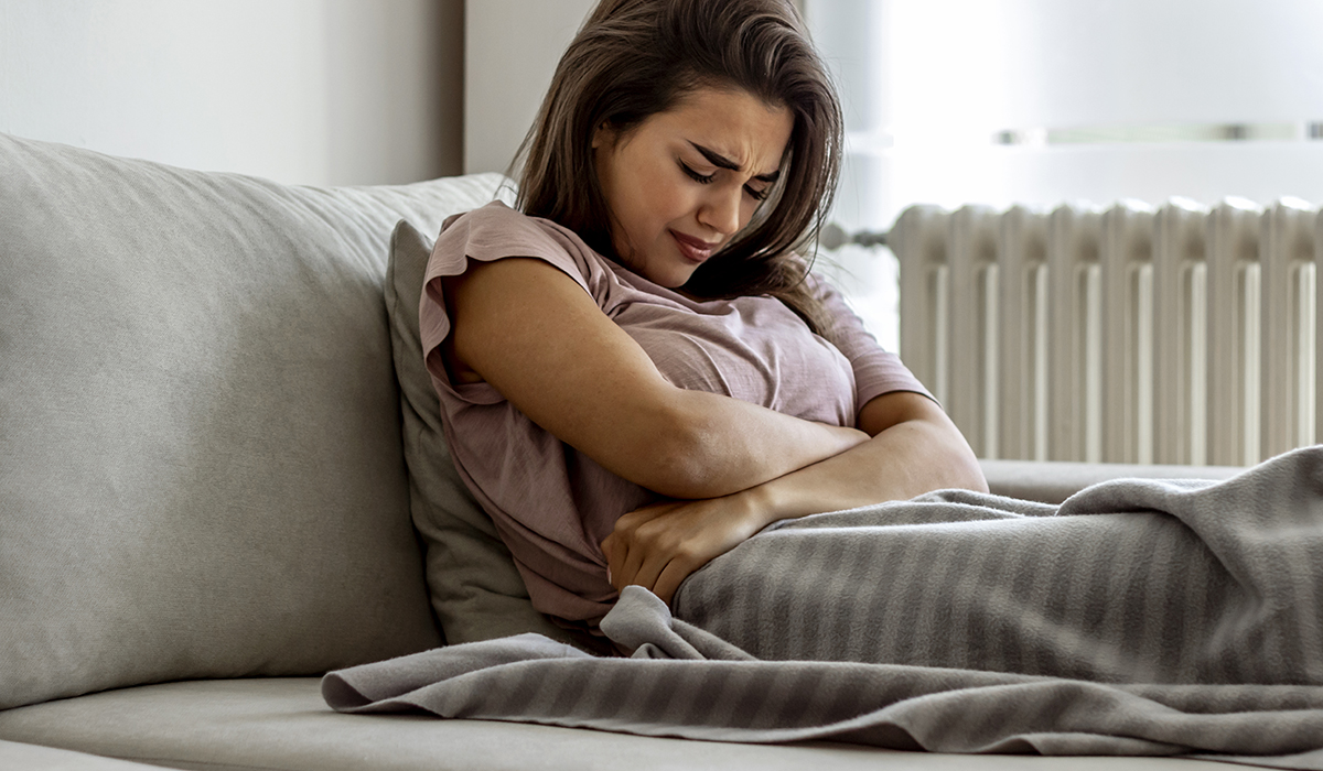 adenomyoosi: nainen istuu sohvalla ja pitelee vatsaansa