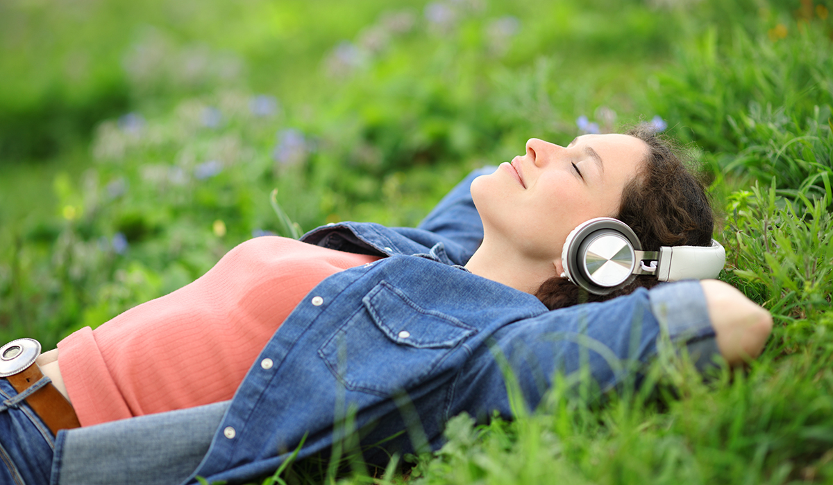 audioartikkeli: nainen makaa kuulokkeet päässä nurmikolla